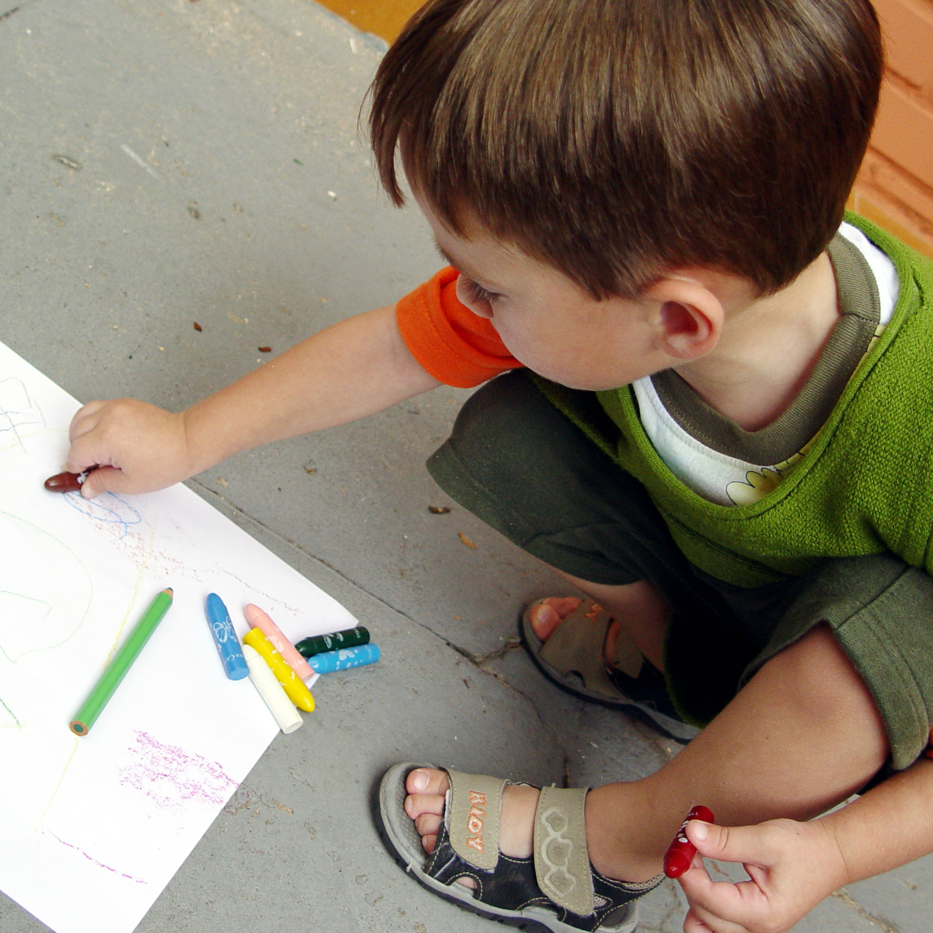 un bambino castano fa un disegno accovacciato per terra