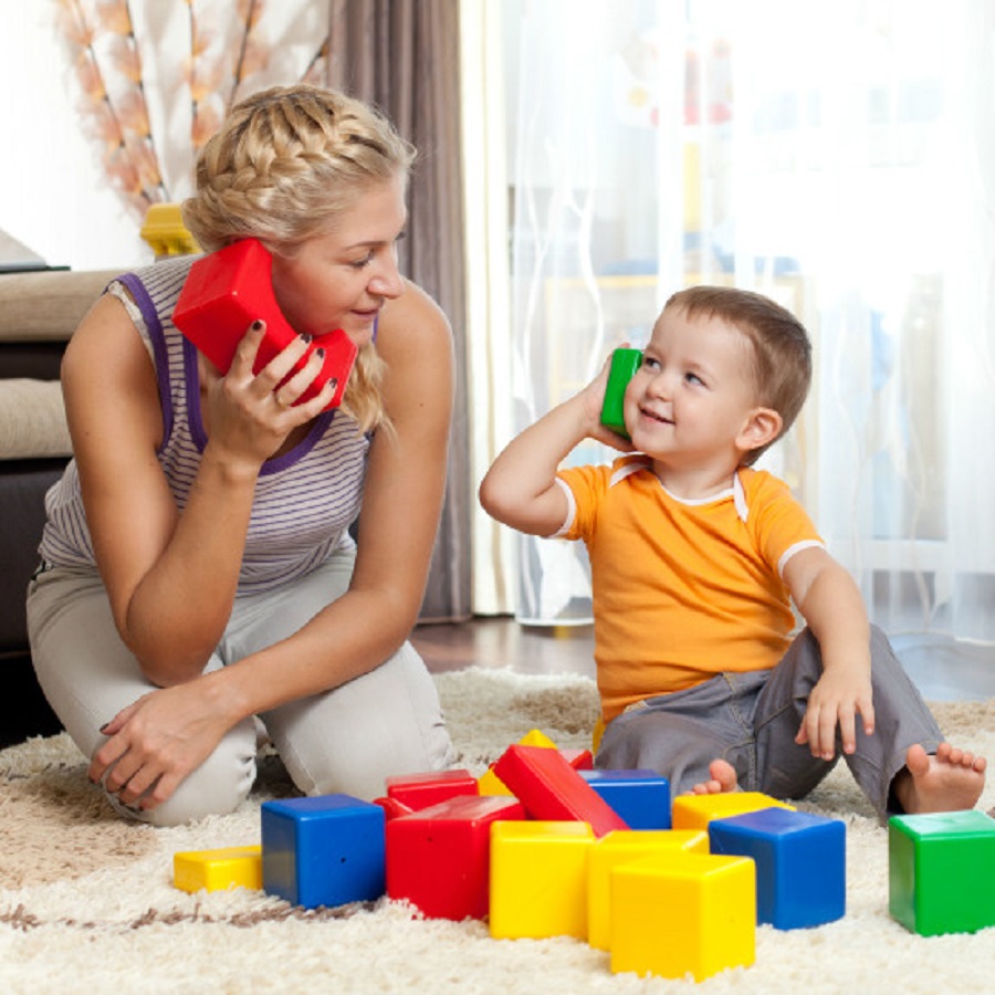 una donna bionda guarda e parla al telefono giocattolo con un bambino biondo