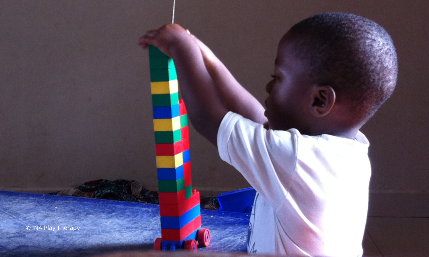 bambino africano seduto fa una piramide con i lego